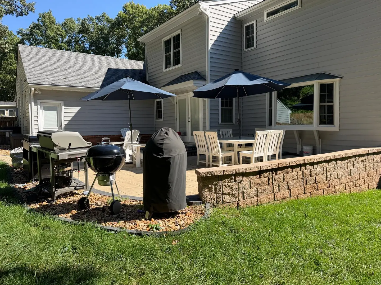 Furnished paver patio with umbrellas, a block retaining wall and surrounding lawn by Willow Landscaping